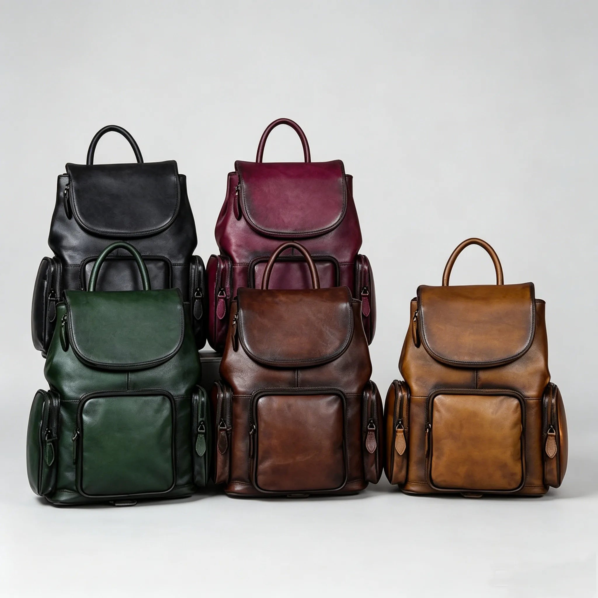 Five leather backpacks in black, burgundy, green, brown, and red on a light gray background.