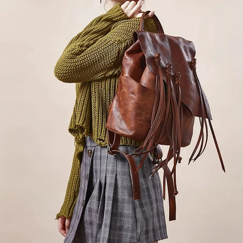 Person wearing a green knitted sweater and gray pleated skirt with a brown leather backpack.
