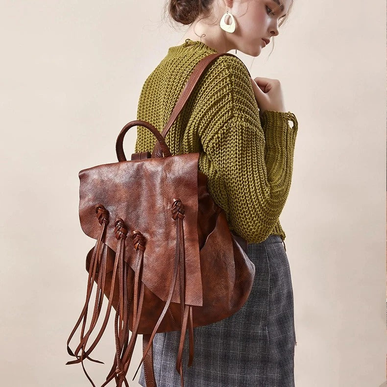 Person wearing a brown leather backpack with decorative straps on a plain background