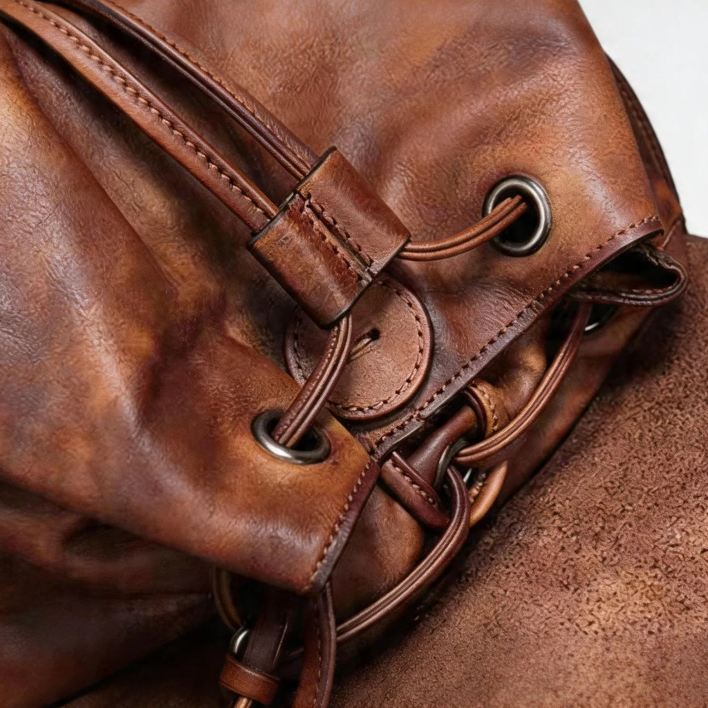 Close-up of a brown leather bag with drawstring closure on a light gray background