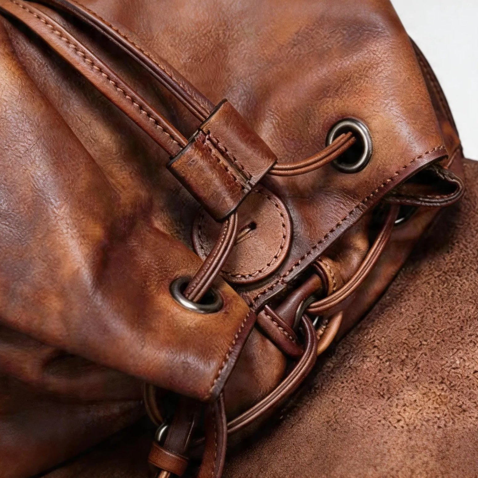 Close-up of a brown leather bag with drawstring closure on a light gray background