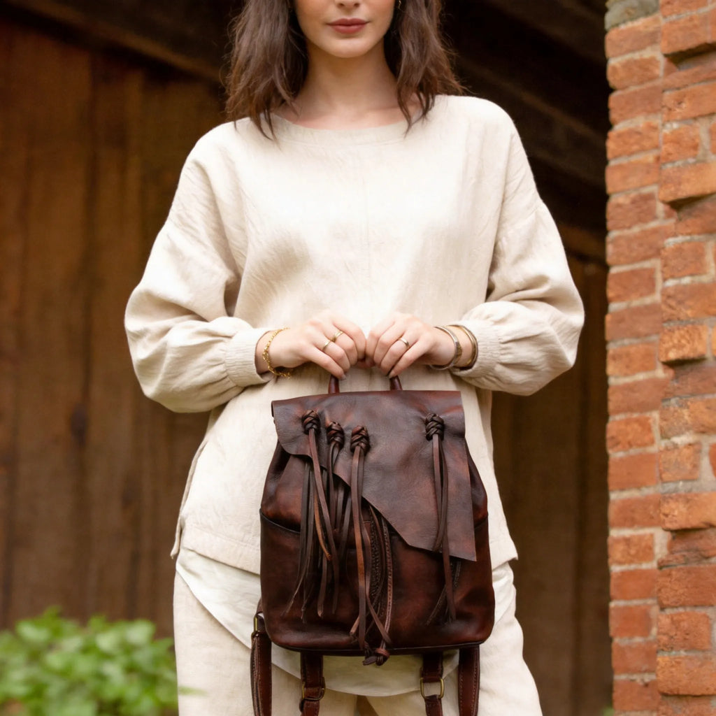 Person holding a brown leather backpack against a rustic background