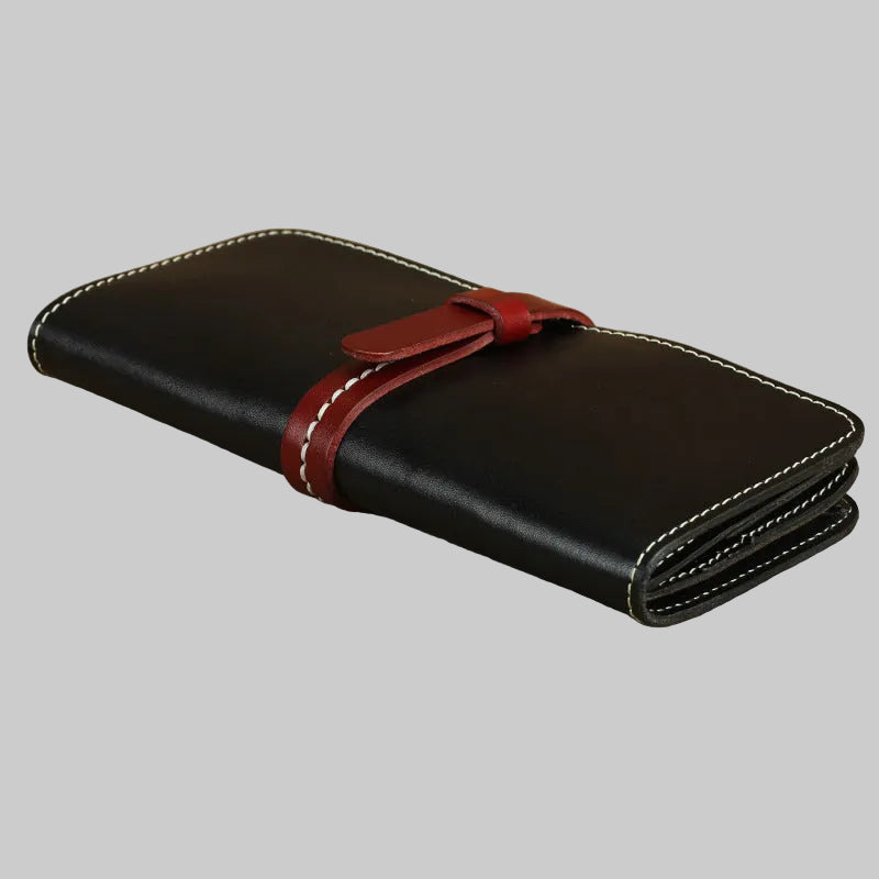 Black leather wallet with a red strap on a beige surface