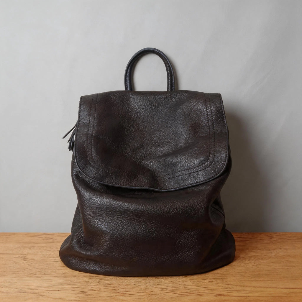 Black leather backpack on a wooden surface with a gray background