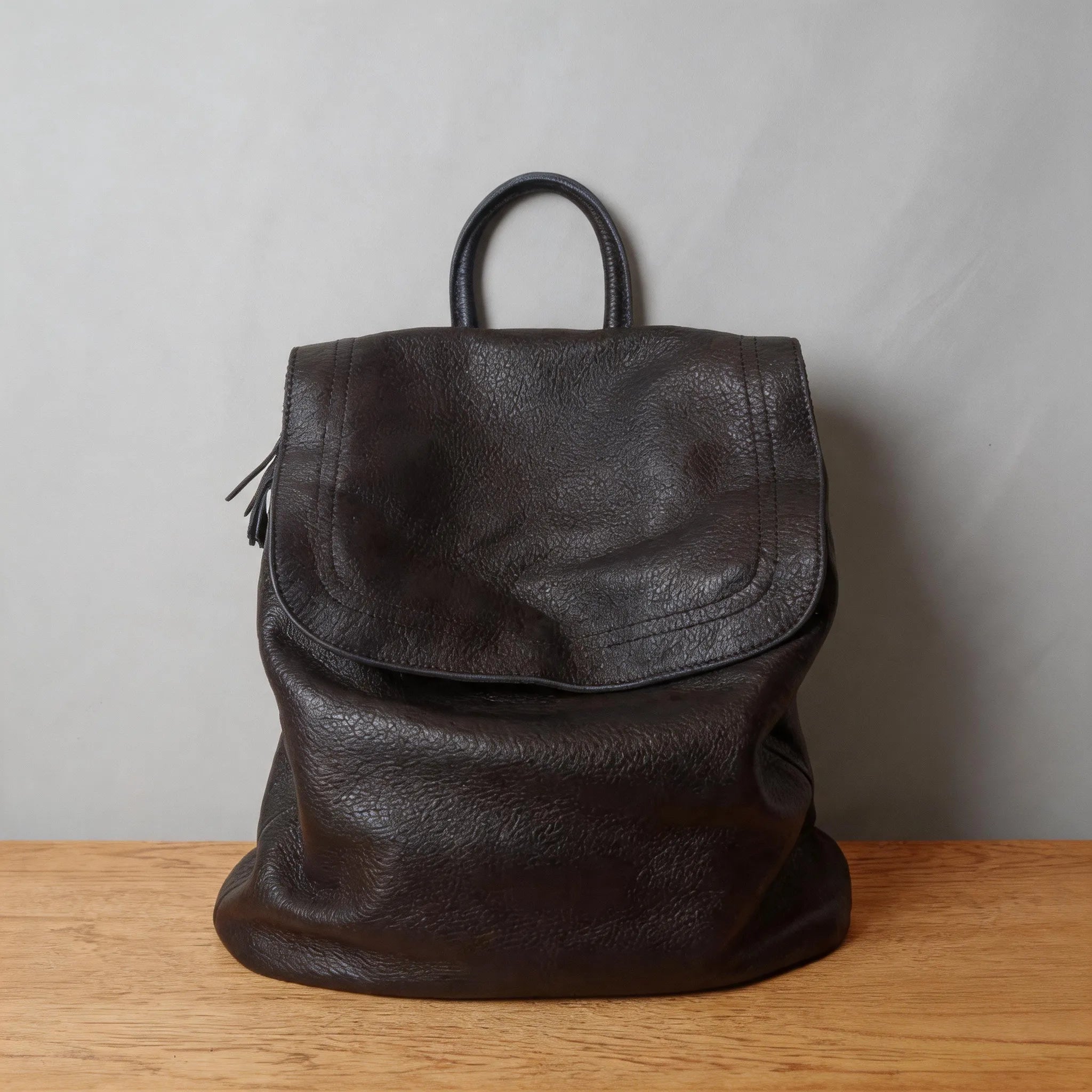 Black leather backpack on a wooden surface with a gray background