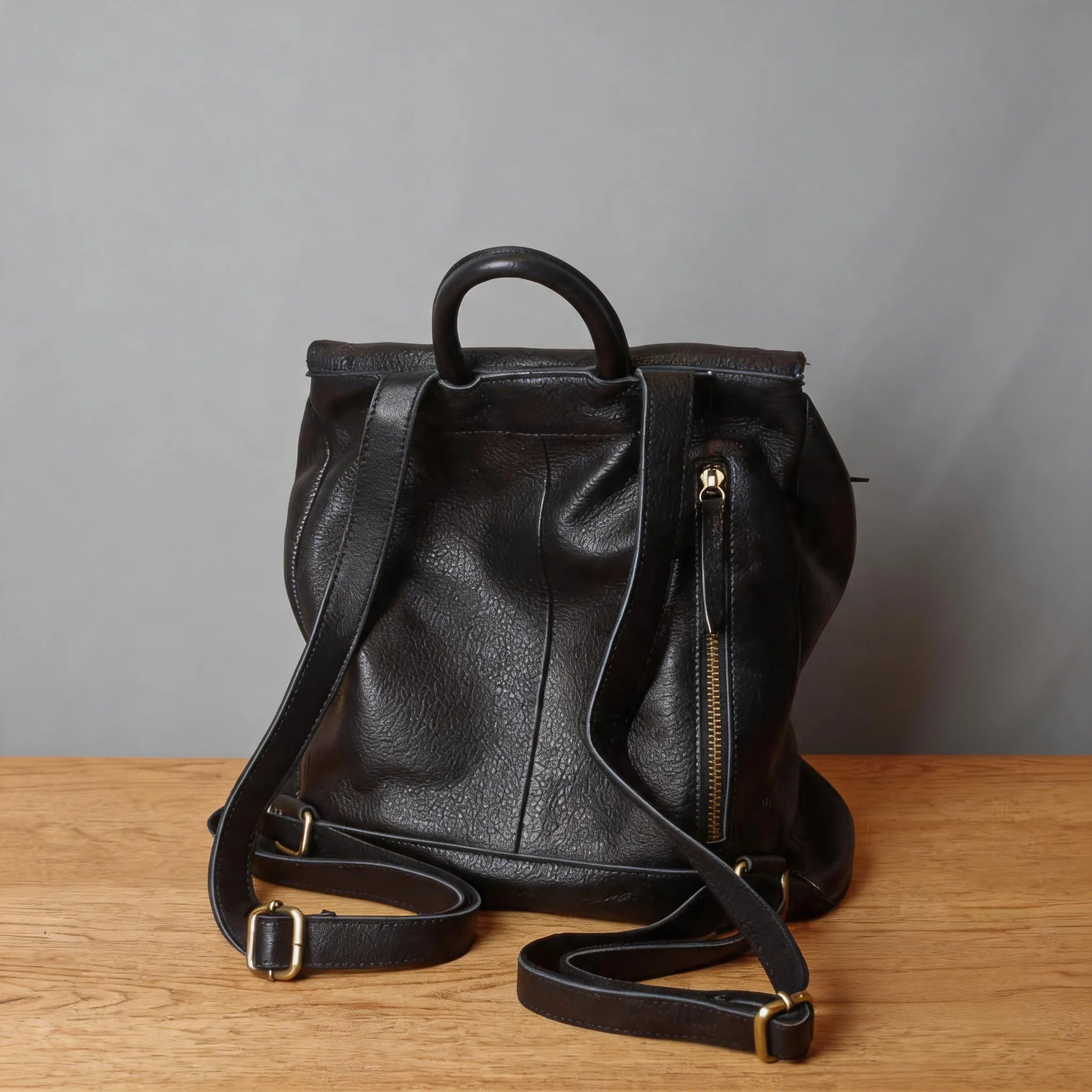 Black leather backpack on a wooden surface with a gray background