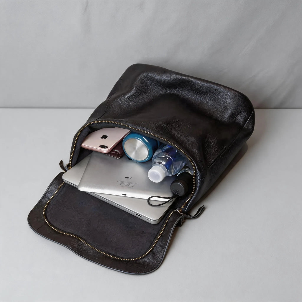 Black leather bag with items like a phone, tablet, and bottles inside on a light gray background