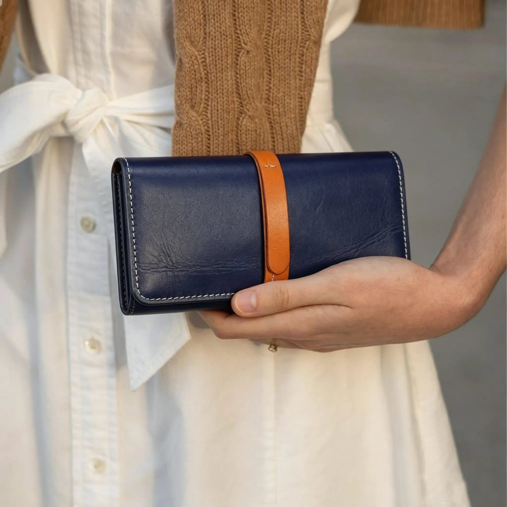 Person holding a navy blue wallet with an orange strap