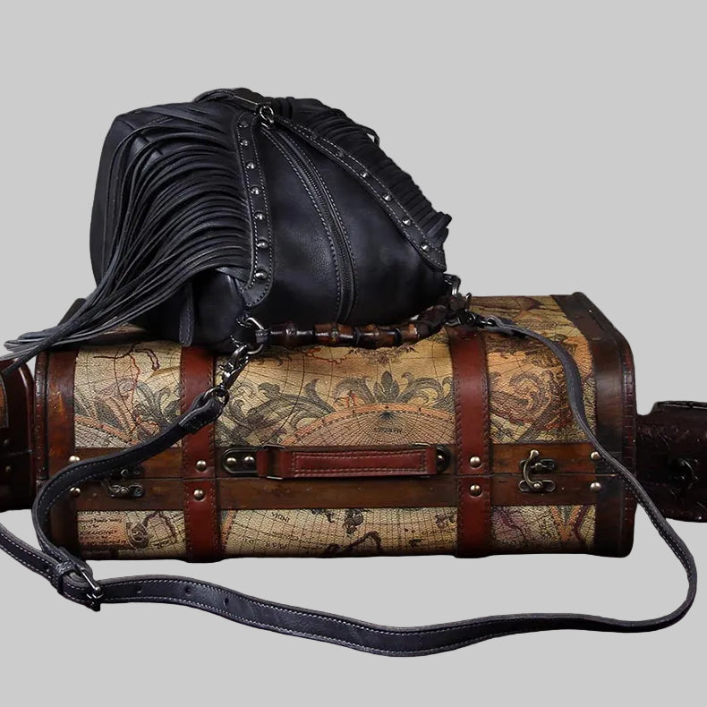 Black leather handbag with fringe details on top of a vintage-style suitcase with world map design.