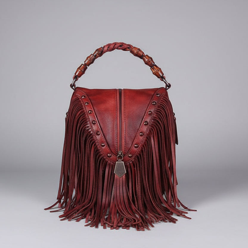 Red leather handbag with fringe and studded details on a gray background