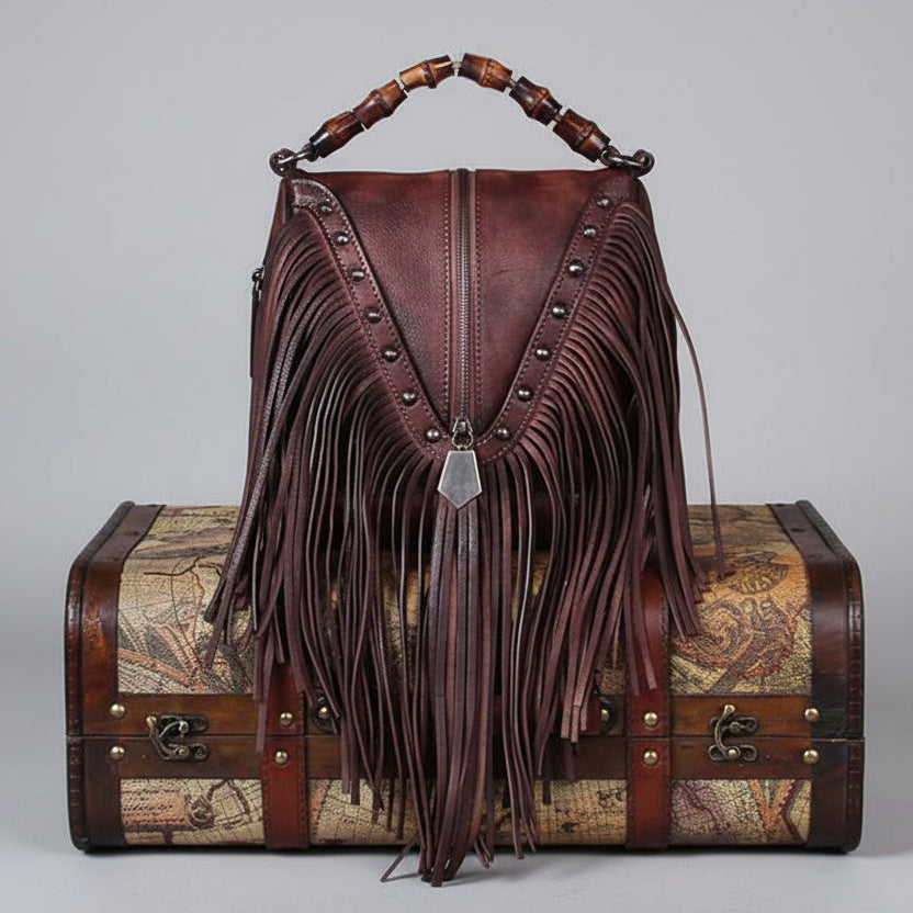 Brown leather bag with fringe and wooden handle on a vintage suitcase