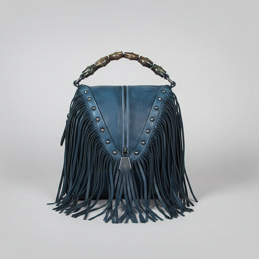 Blue suede handbag with fringe and studded details on a light gray background