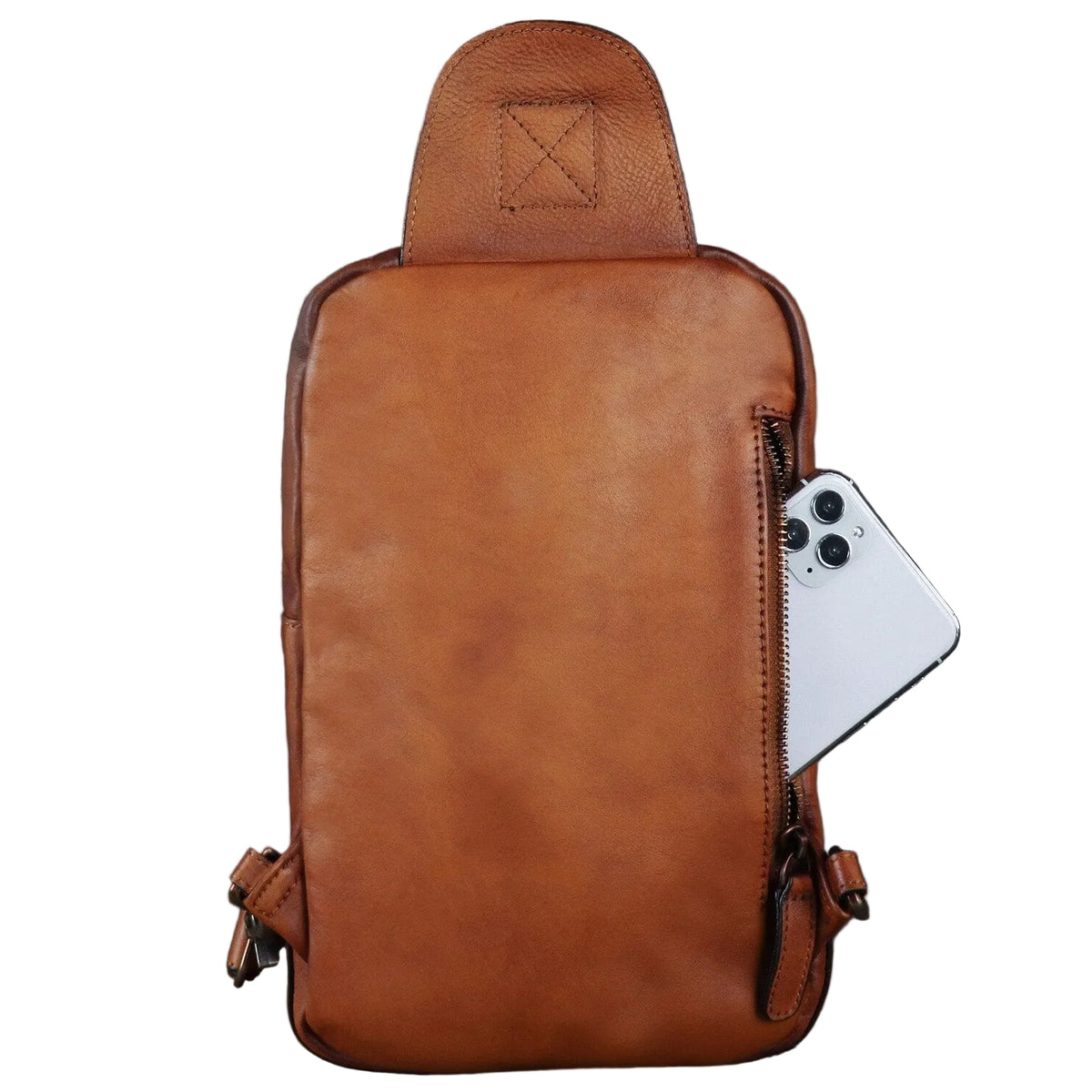 A brown leather crossbody backpack with a top handle, shown with a white smartphone tucked into its side zip pocket against a dark gray background.