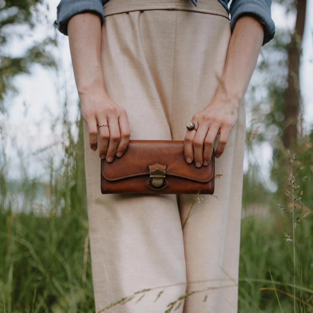 Person holding a brown leather clutch in a natural setting