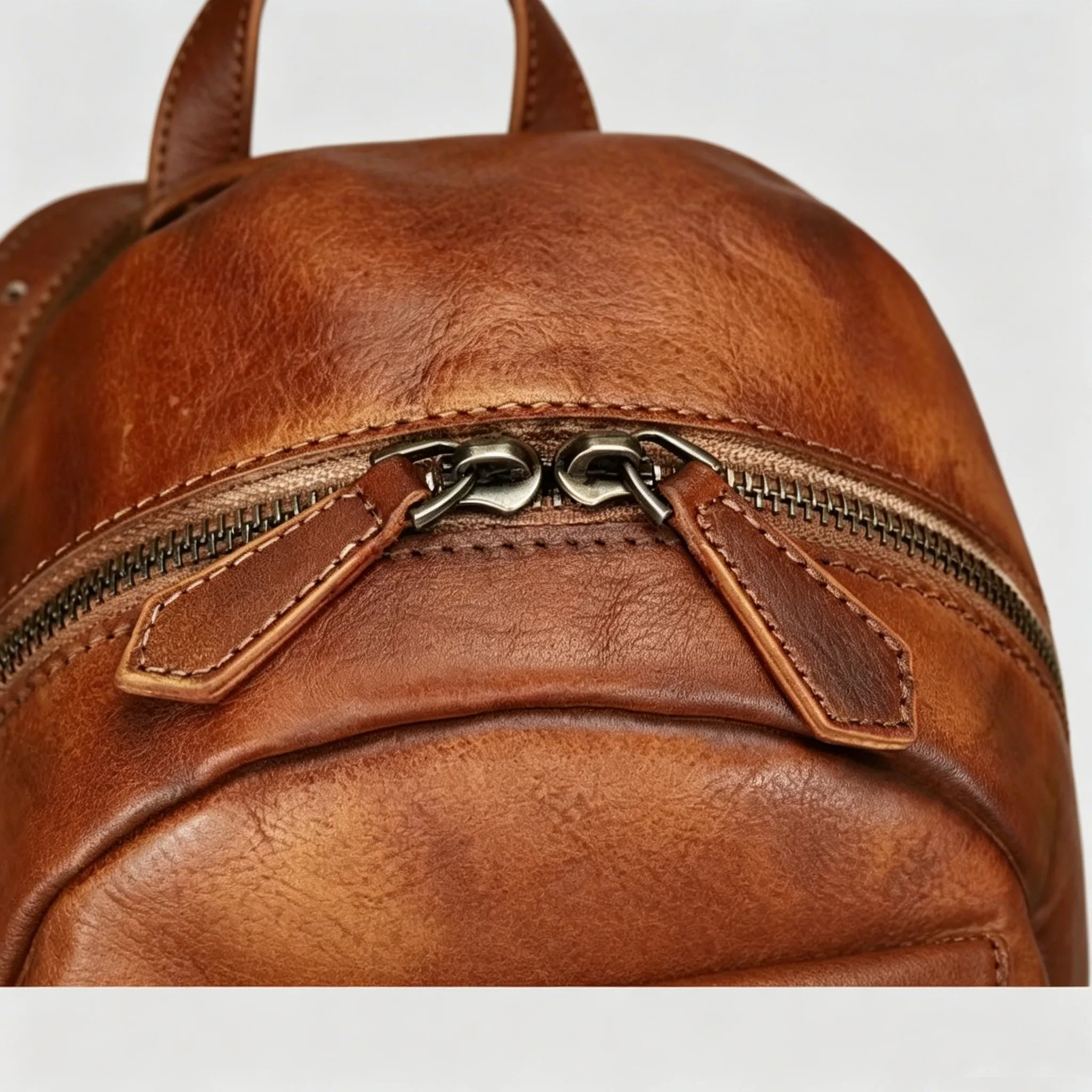 Brown leather backpack with a zipper on a light gray background
