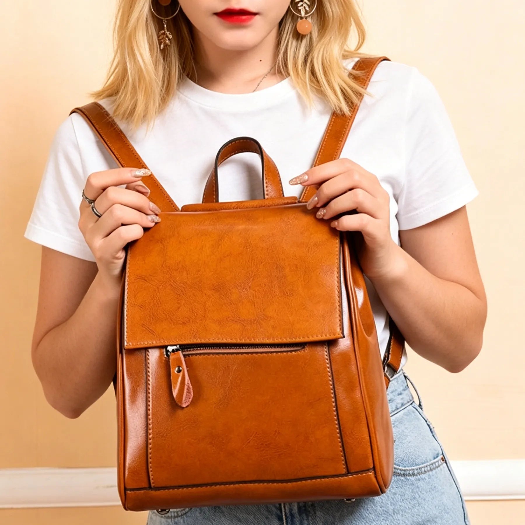 Person holding a brown leather backpack against a beige background