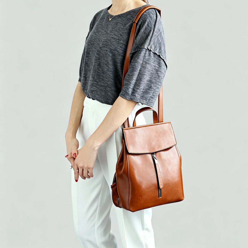 Person holding a brown leather backpack against a plain background