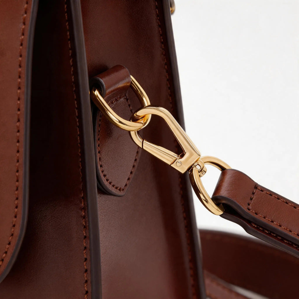 Close-up of a brown leather handbag with a gold clasp on a white background