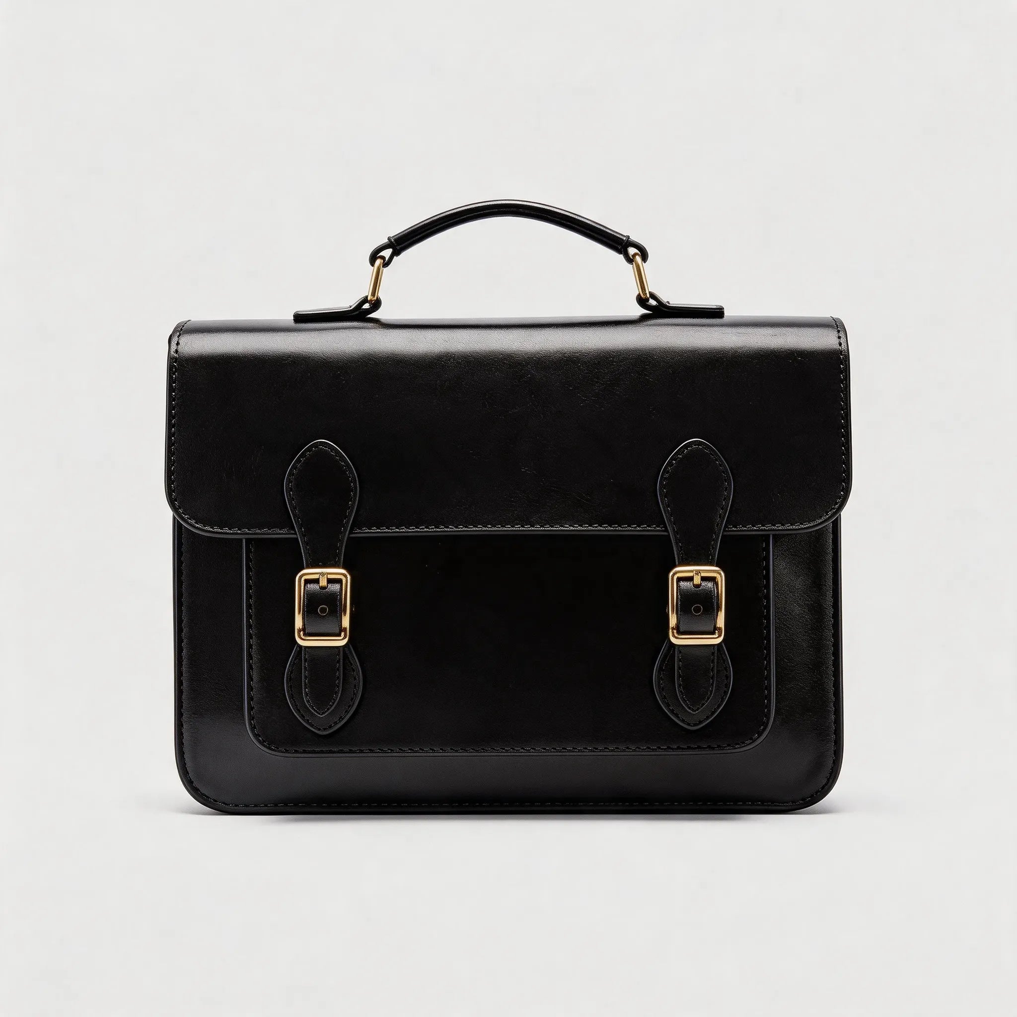 Black leather satchel with gold buckles on a light gray background