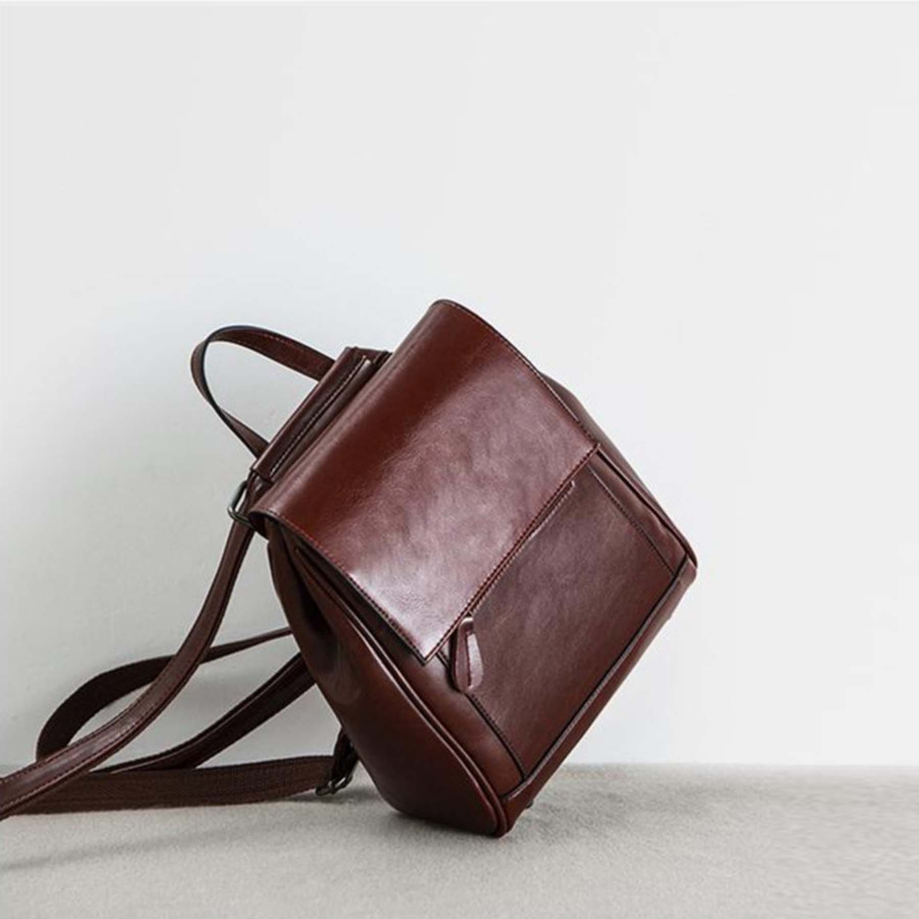 Brown leather backpack on a light gray surface with a white background