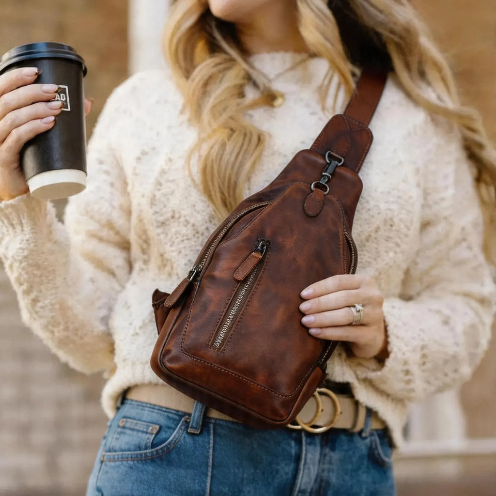 Person holding a brown leather sling bag and a coffee cup.