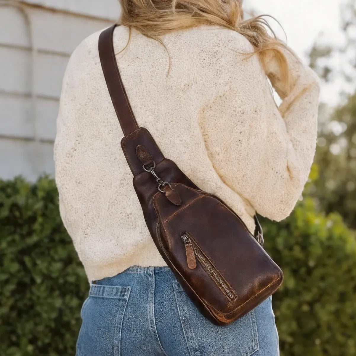 Person wearing a brown leather sling bag with a blurred outdoor background