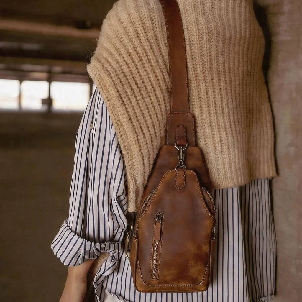 Person wearing a beige knit poncho over a striped shirt with a brown leather bag.