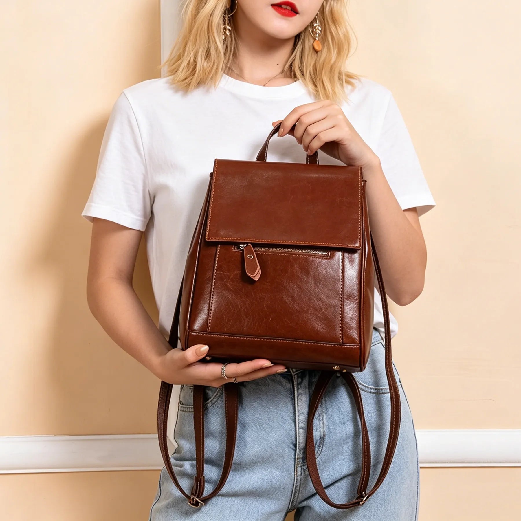Person holding a brown leather backpack against a beige wall