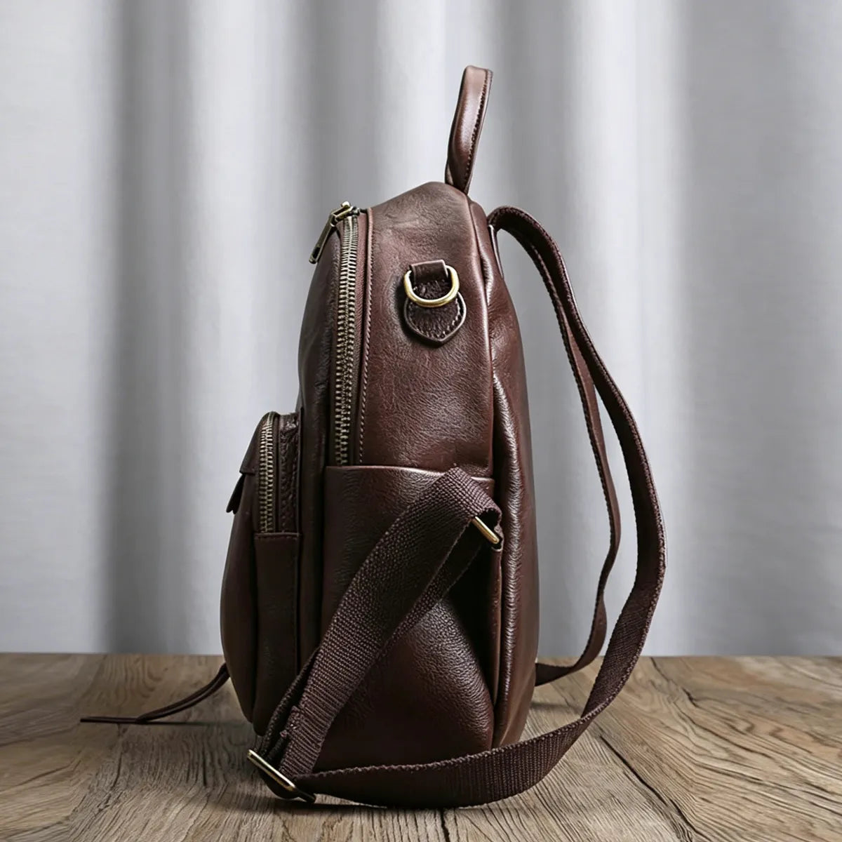 Brown leather backpack on a wooden surface with a gray curtain background