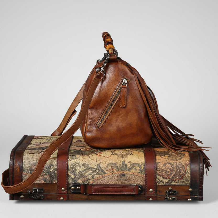 Brown leather bag with fringes on top of a vintage-style suitcase with world map design.