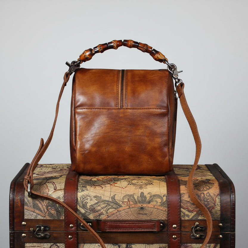 Brown leather handbag with decorative handle on a vintage suitcase with world map design.
