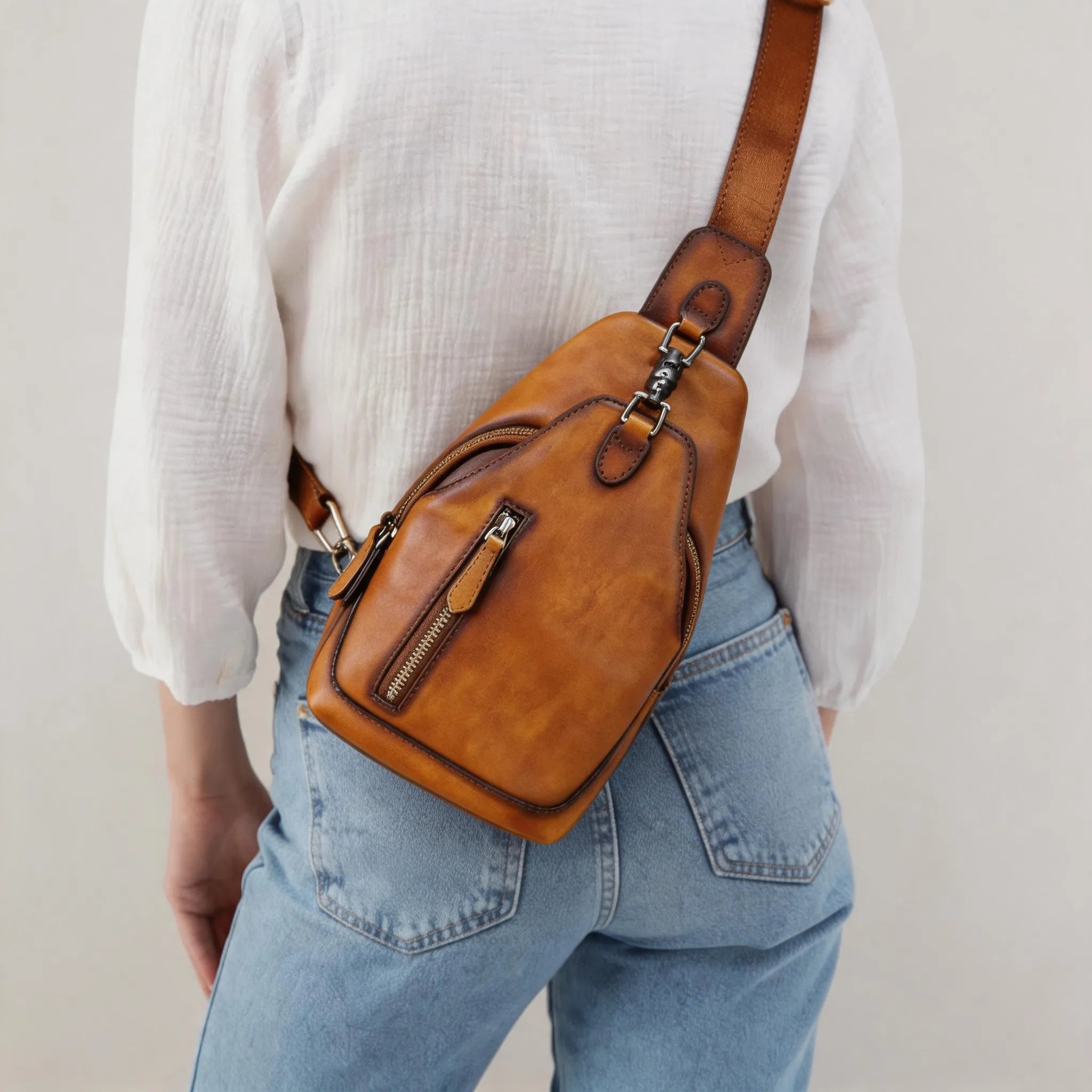 Person wearing a brown leather sling bag over shoulder against a plain background