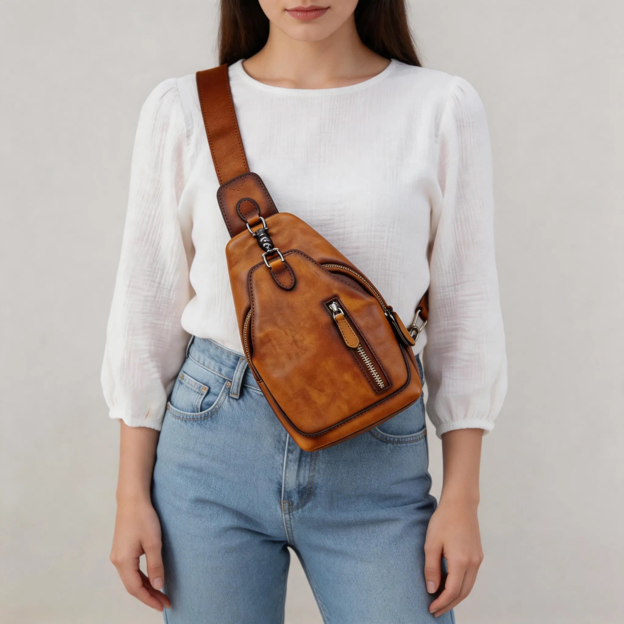 Person wearing a brown leather crossbody bag with a plain background