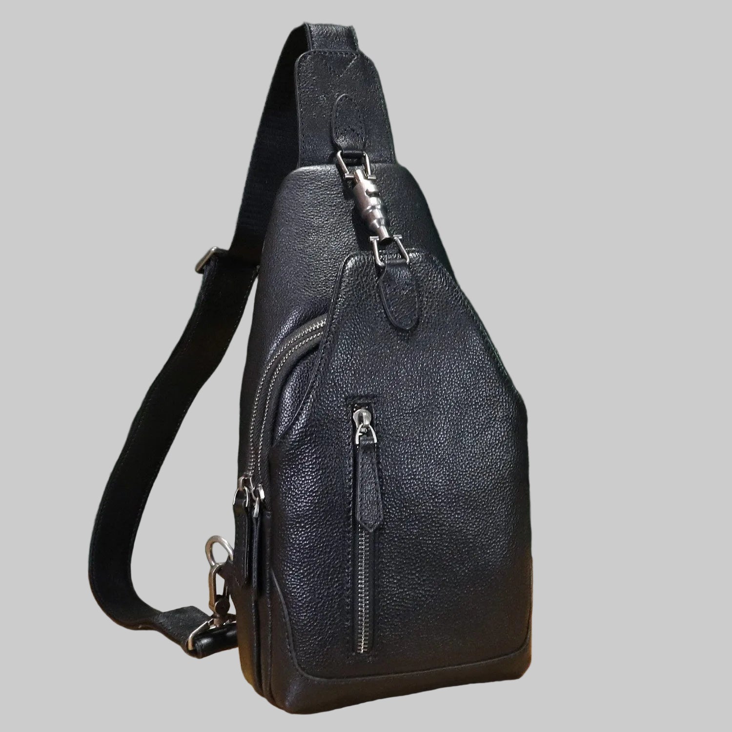 Black leather sling bag with zippers on a gray background