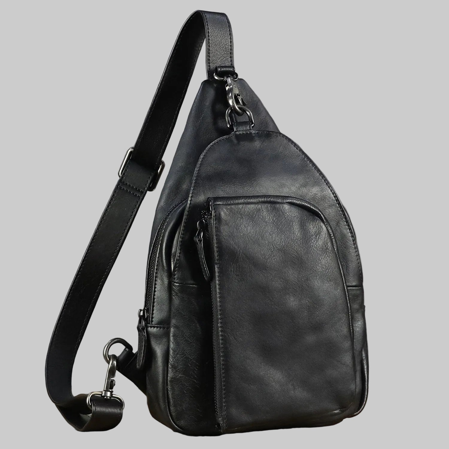 Black leather sling bag on a wooden surface with a gray background