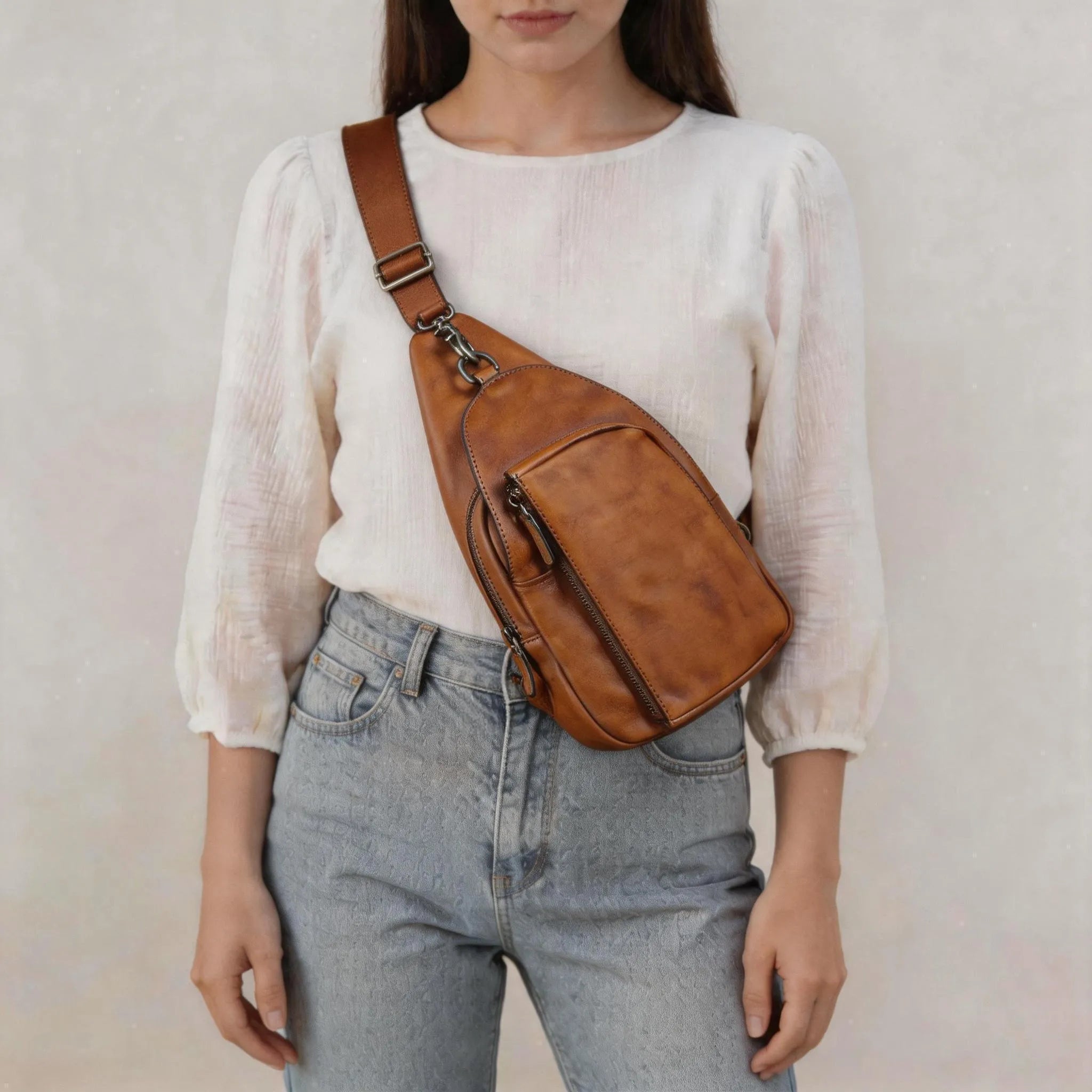 Person wearing a brown leather sling bag over one shoulder against a plain background