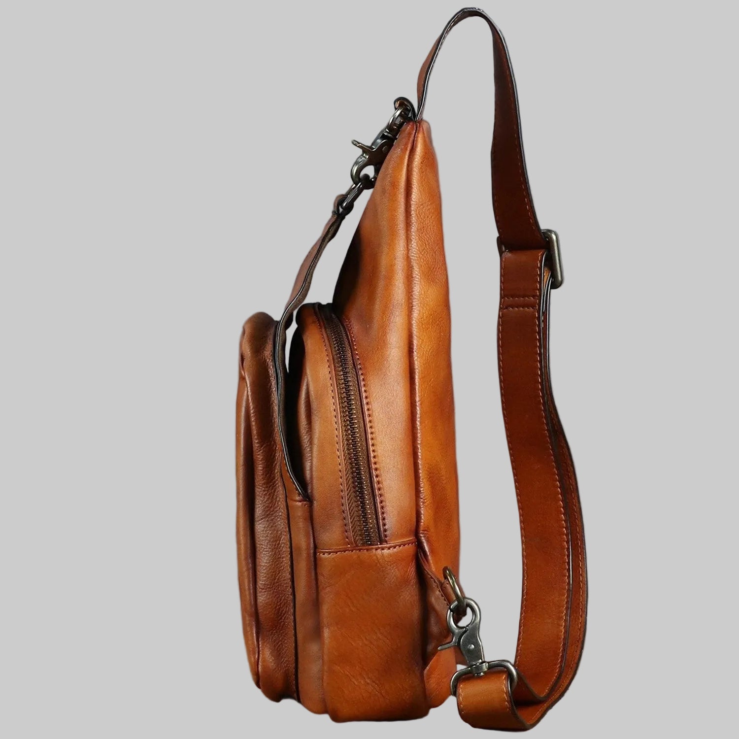 Brown leather sling bag on a textured surface with a gray background