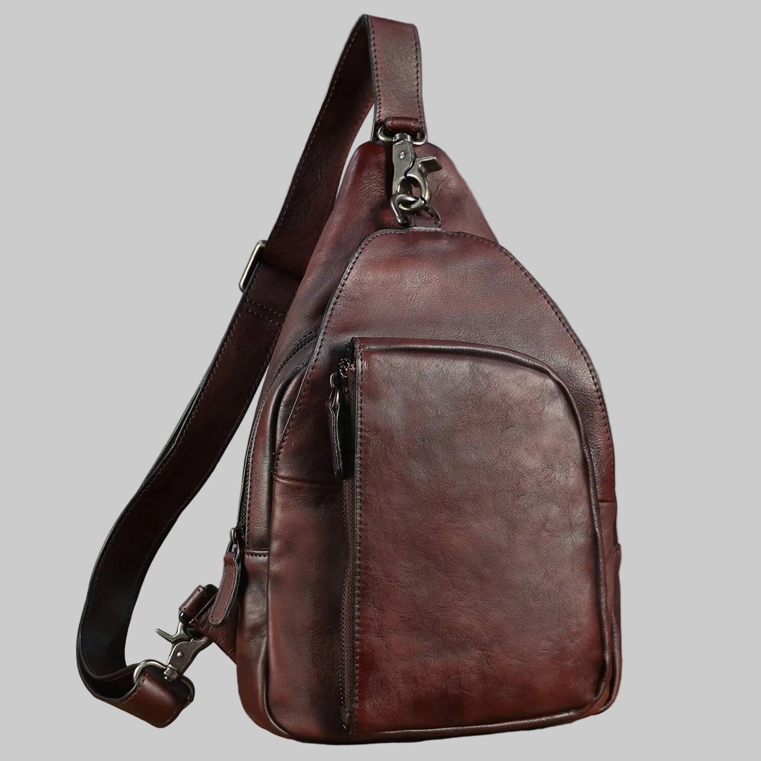 Brown leather sling bag on a wooden surface with a gray background