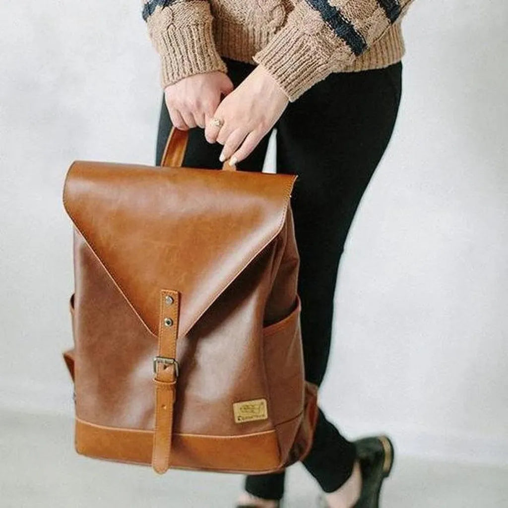 Person holding a brown leather backpack against a plain background