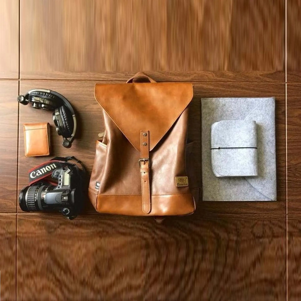 Brown leather backpack with camera, wallet, and other items on a wooden surface