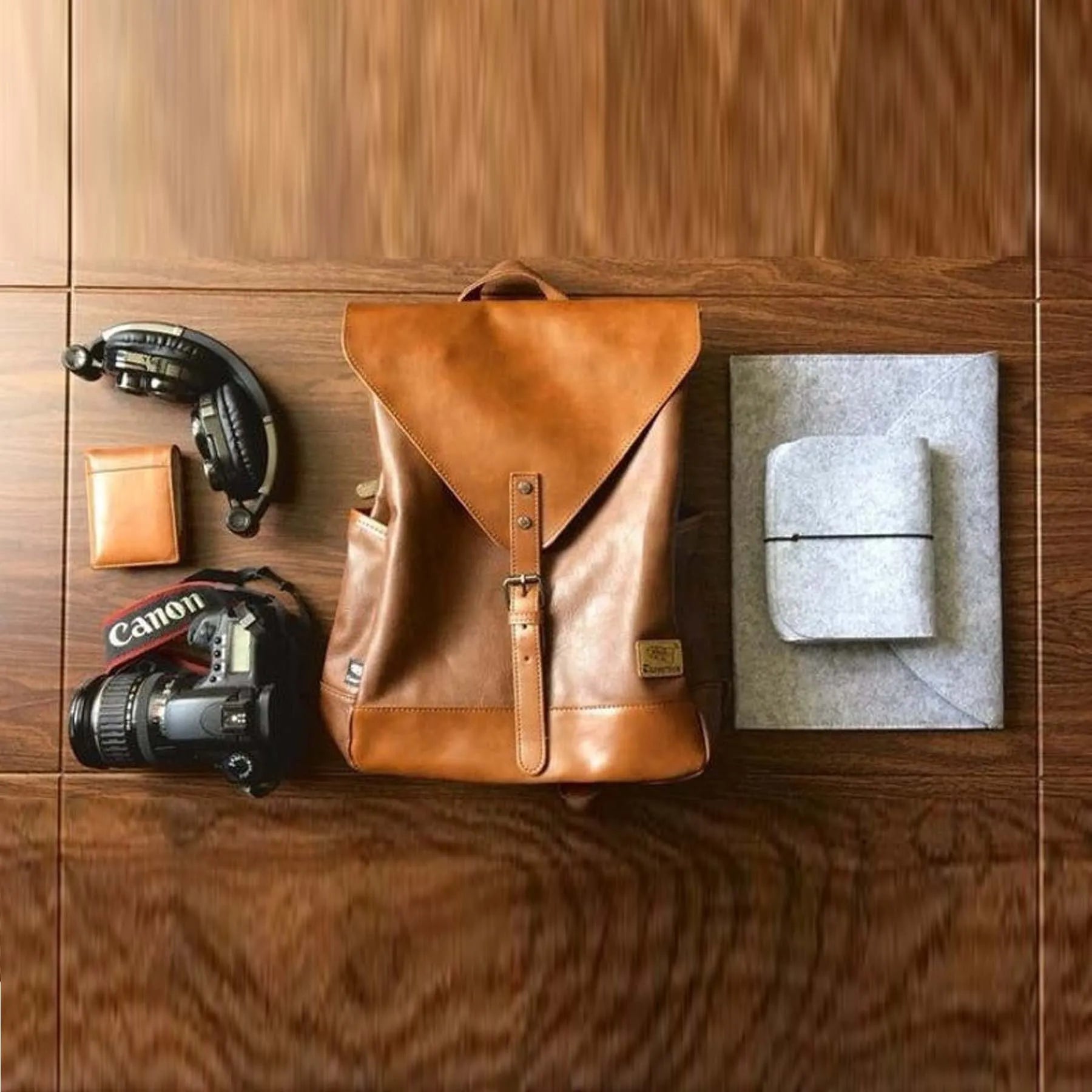 Brown leather backpack with camera, wallet, and other items on a wooden surface