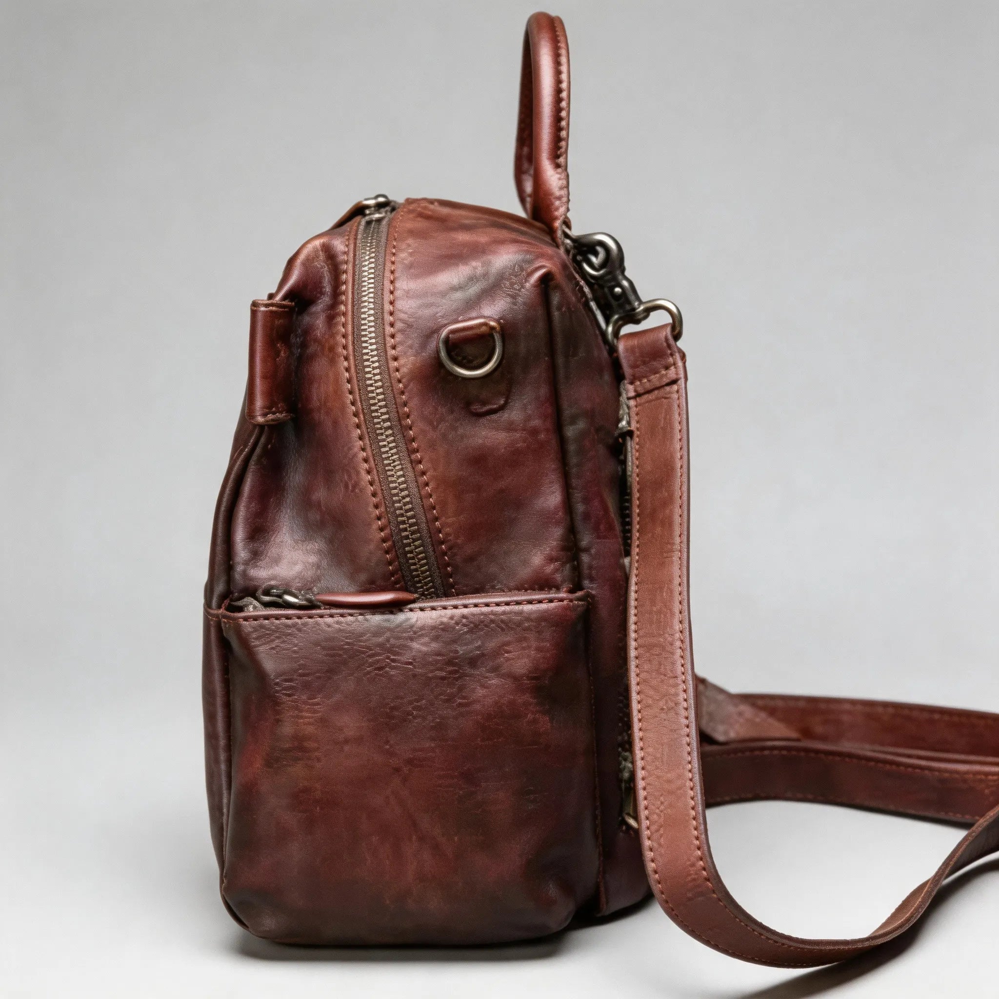 Brown leather backpack with a strap on a light gray background