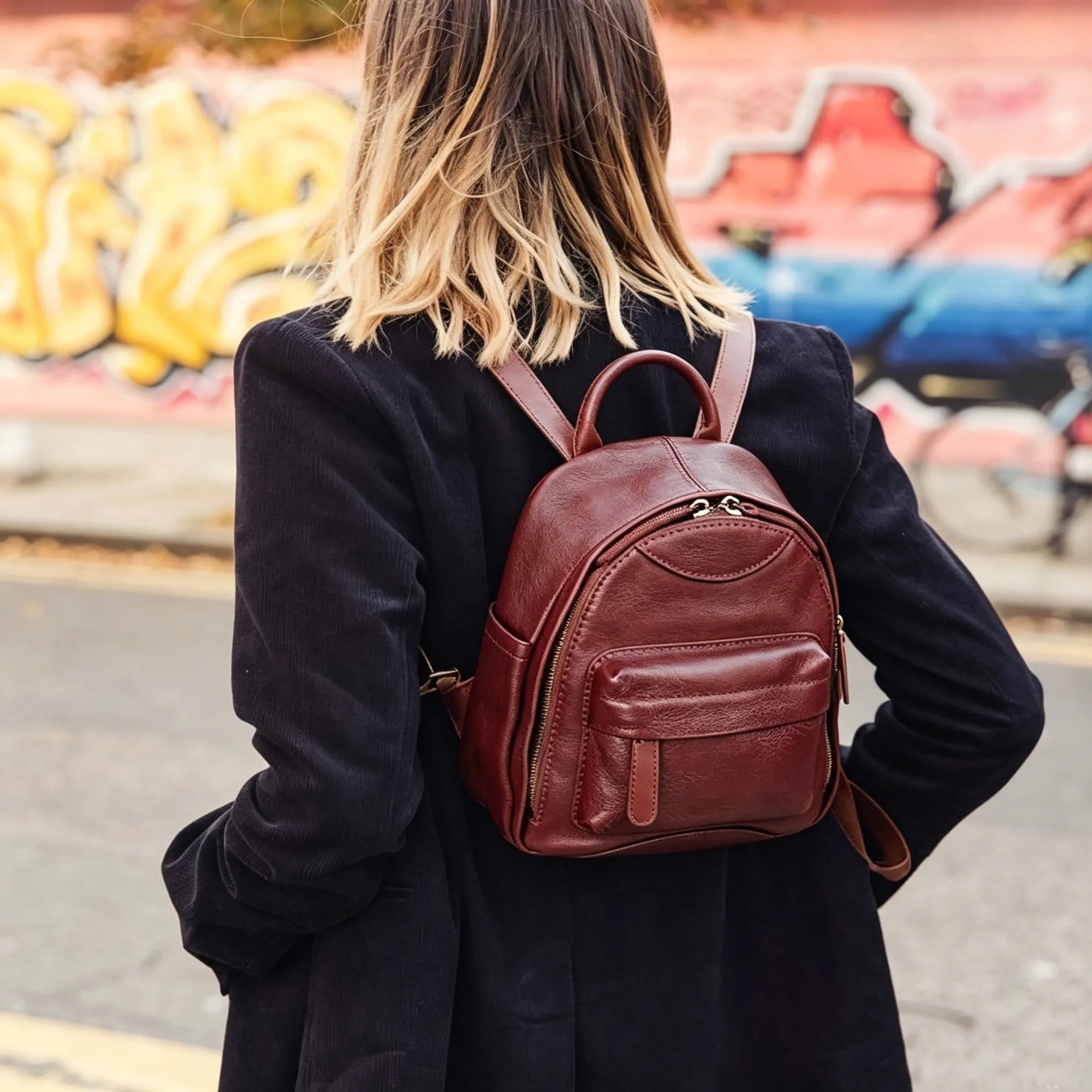 Person wearing a brown leather backpack with a graffiti-covered wall in the background