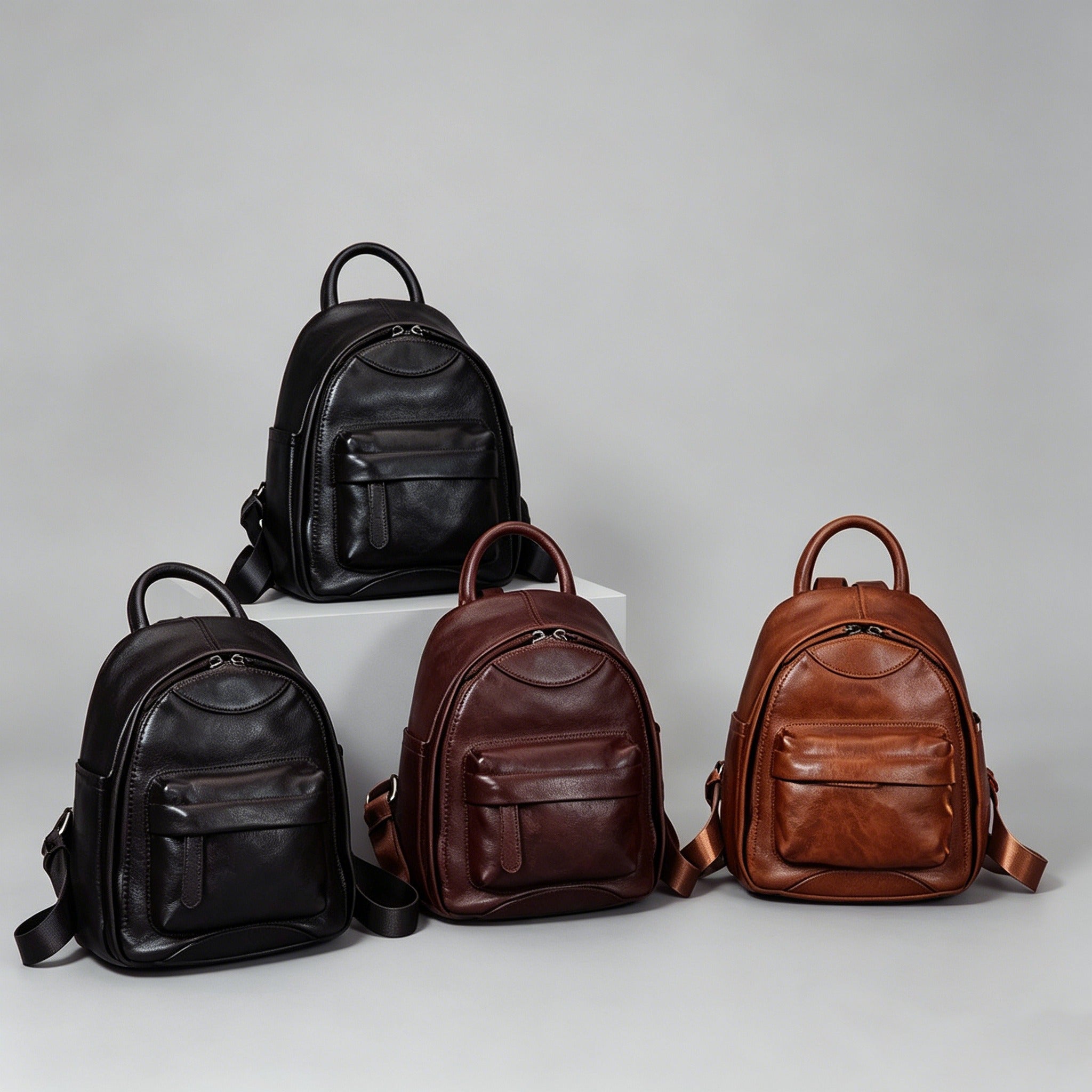 Four leather backpacks in black, brown, and dark brown on a gray background