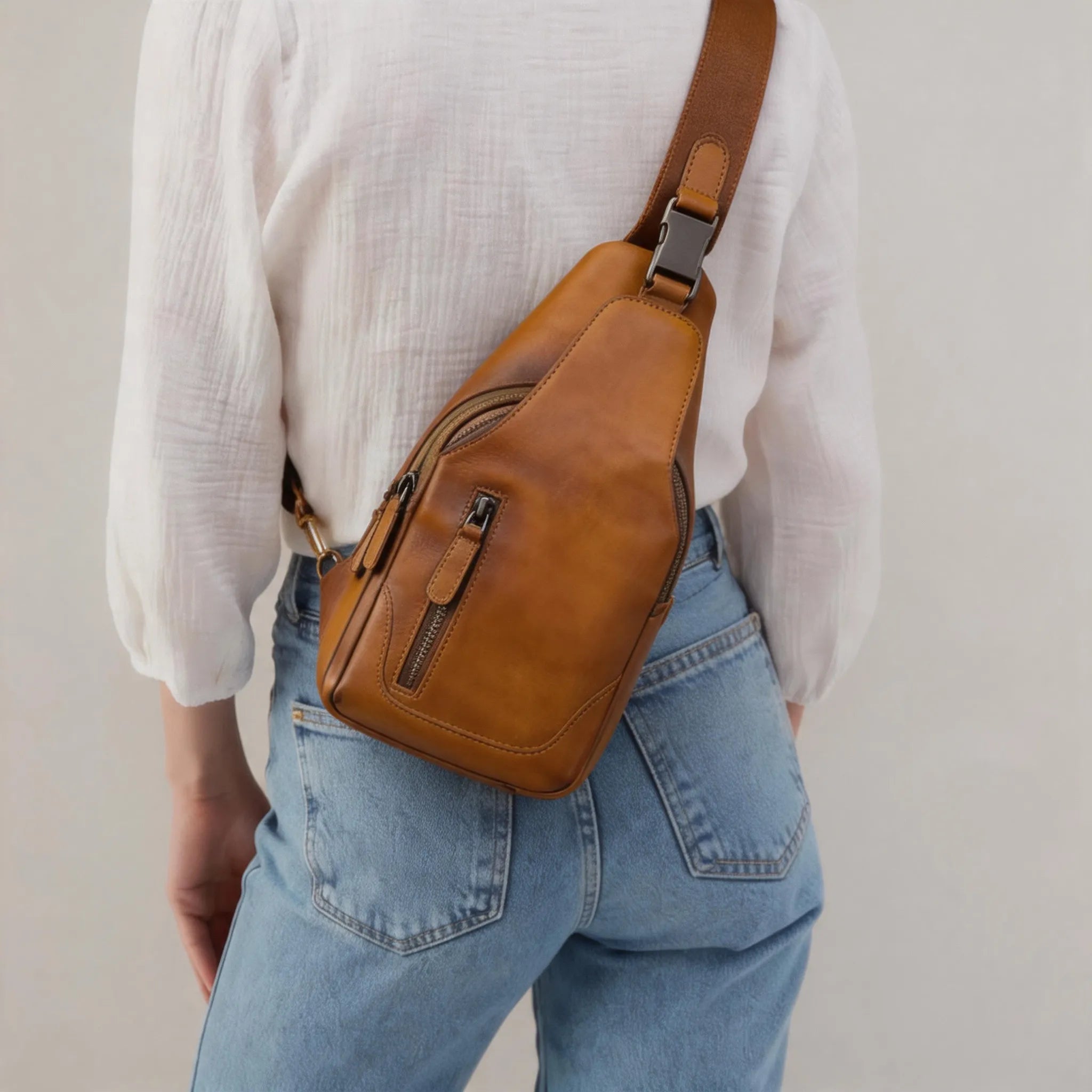 Person wearing a brown leather crossbody bag with a plain background