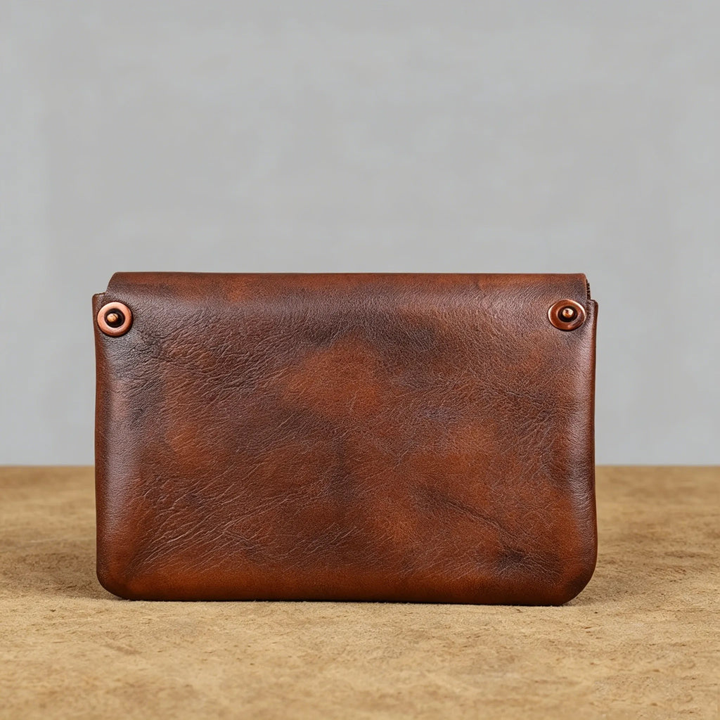 Brown leather pouch with copper rivets on a wooden surface and gray background