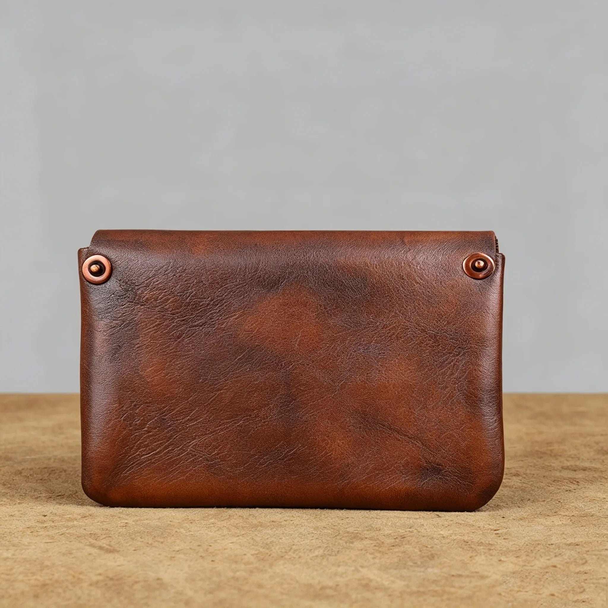 Brown leather pouch with copper rivets on a wooden surface and gray background