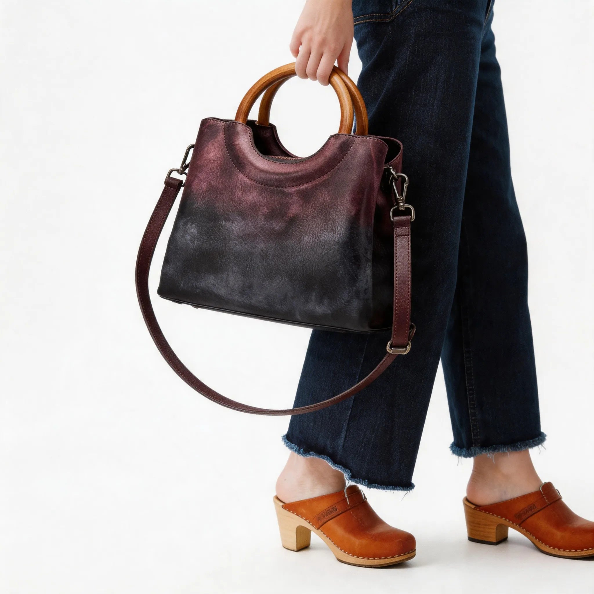 Person holding a brown leather handbag with wooden handle on a white background