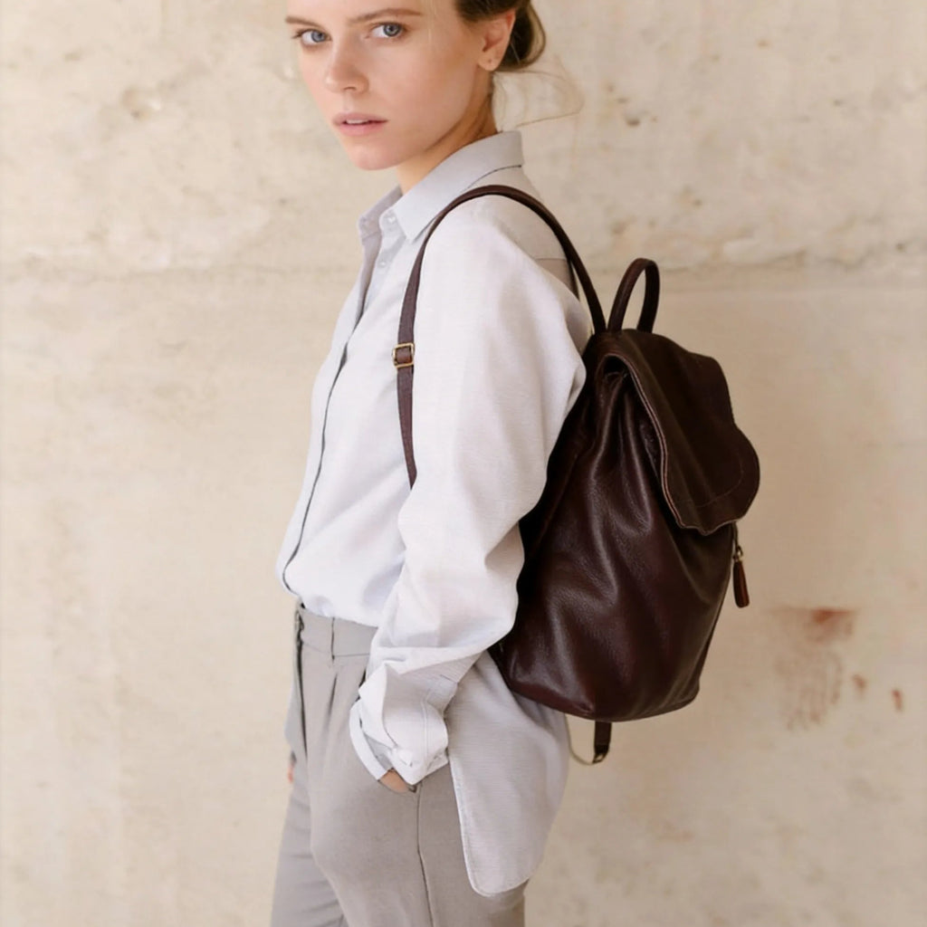 Woman wearing a brown leather backpack against a plain background