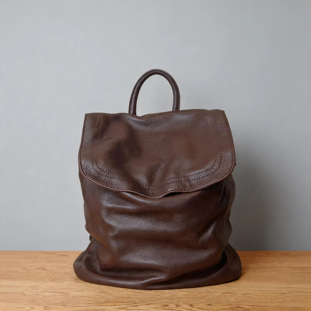 Brown leather backpack on a wooden surface with a gray background
